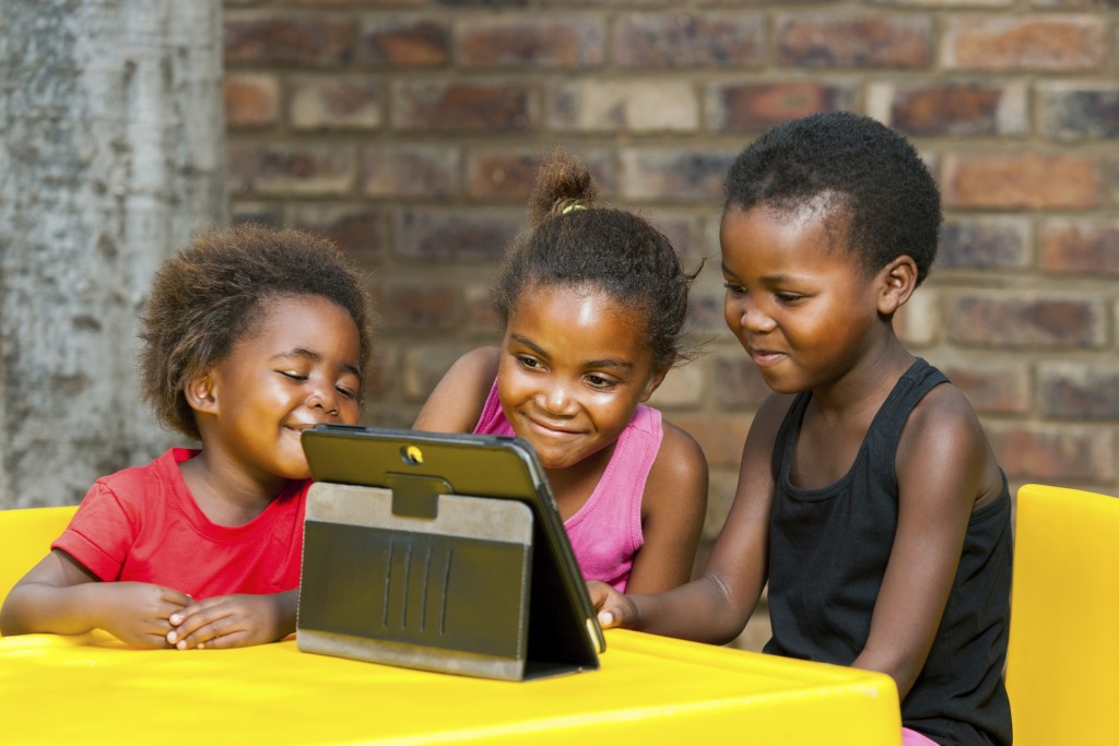 Three african kids playing together on tablet.
